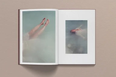 An open book displaying two photographic spreads featuring figures floating in water on a textured background.