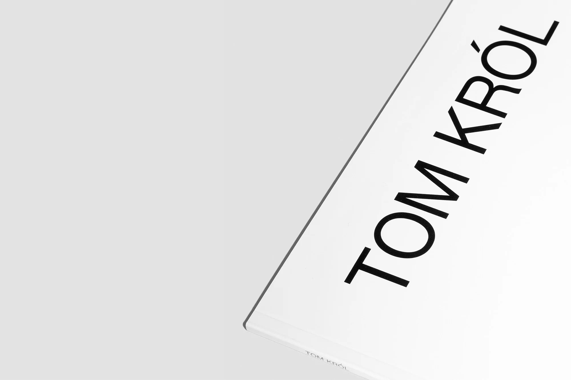 Black typography spelling TOM KROL set against a clean white paper texture surface with subtle shadow detail.