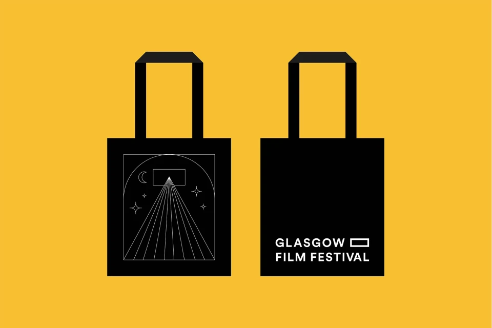 Two black tote bags are displayed against a yellow background, one featuring a white graphic design, the other showing the 'Glasgow Film Festival' logo.