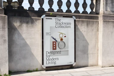 An outdoor advertising poster for ENSEMBL Stackware Collection mounted on a stone wall beneath a classic balustrade.
