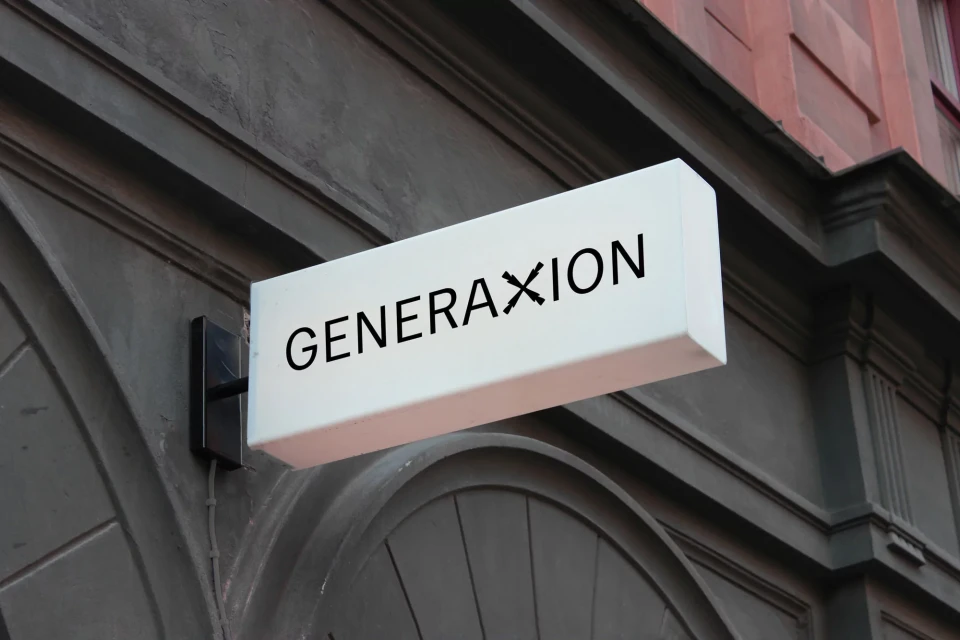 Illuminated GENERAXION sign mounted on the exterior wall of a building, featuring a modern logo against a dark grey facade.
