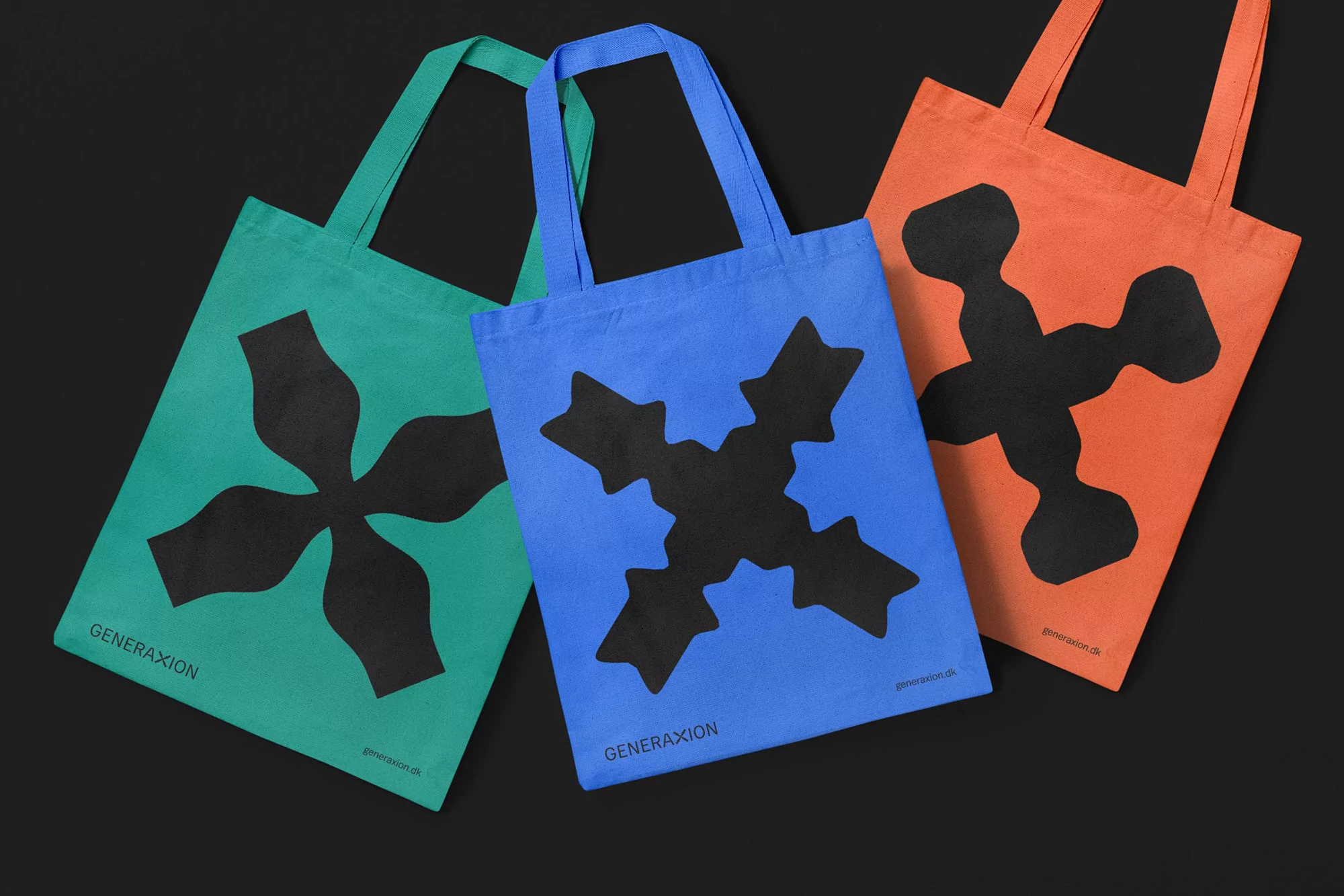 Three tote bags in green, blue, and orange with black graphic prints are laid out against a black background.