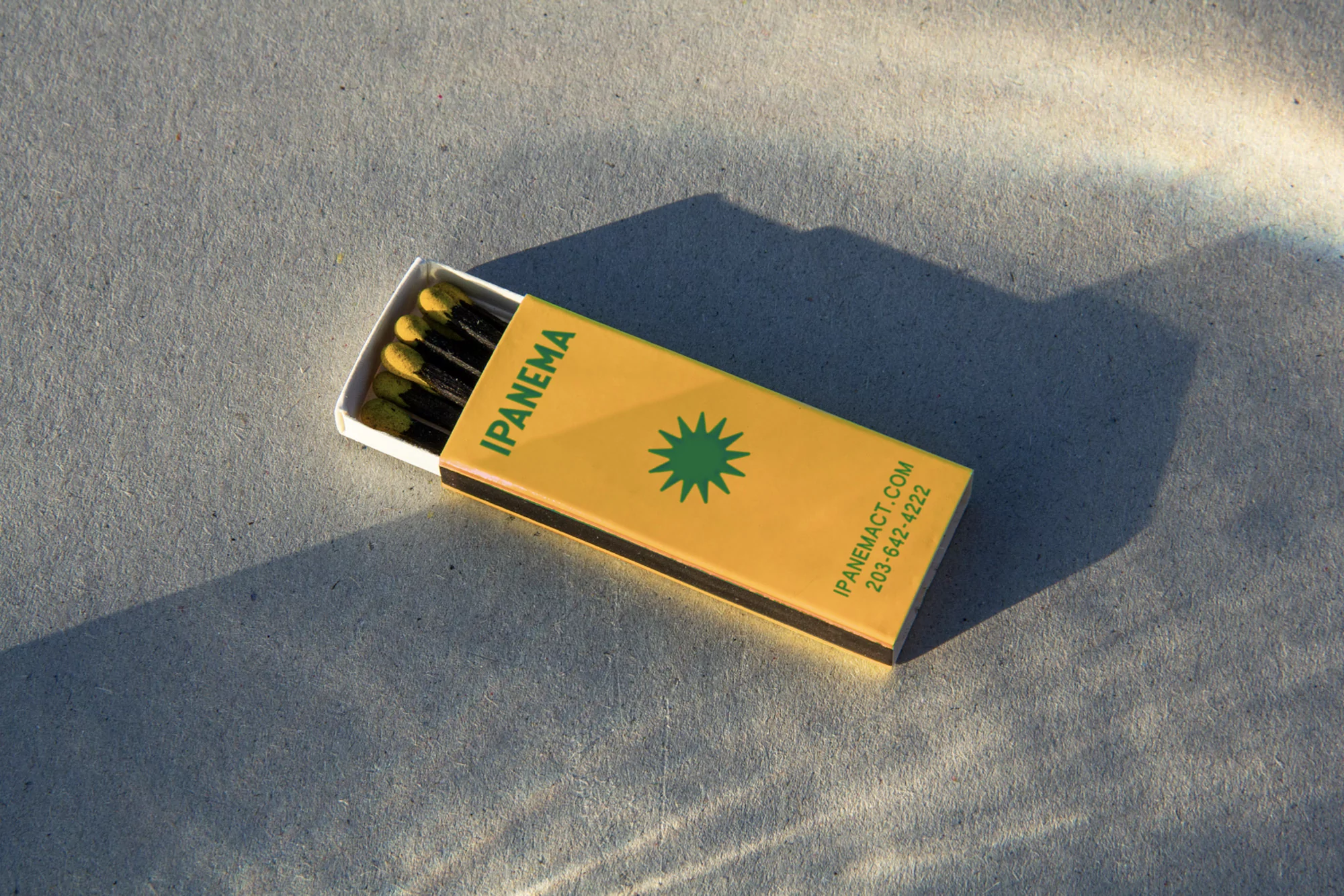 Open matchbox with black matches on a concrete surface, illuminated by sunlight, creating shadows and highlights around the box.