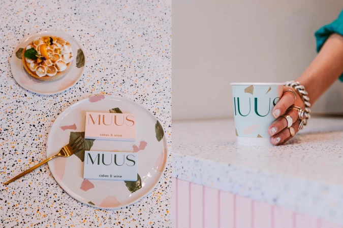 Overhead shot of Muus cafe setting with desserts, gold fork, coffee cup, brand cards on a patterned table with a customer.