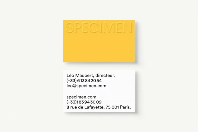 Two business cards on a white background. One is yellow with embossed text 'SPECIMEN' and the other is white with black contact information.