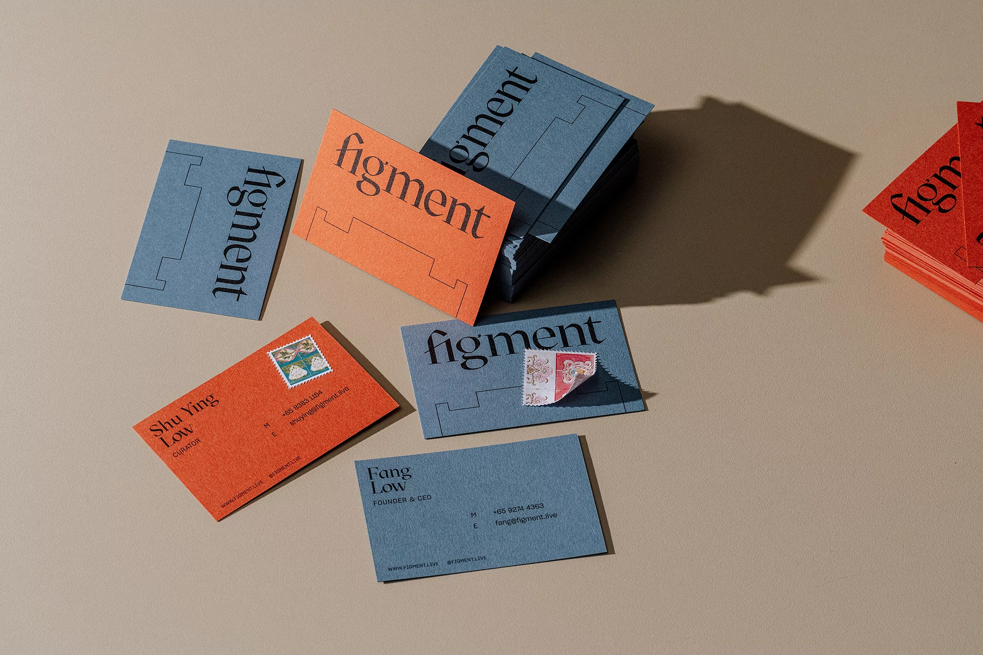 Arrangement of business cards in red and blue, with clean typography and minimalist design, placed on a light brown surface.