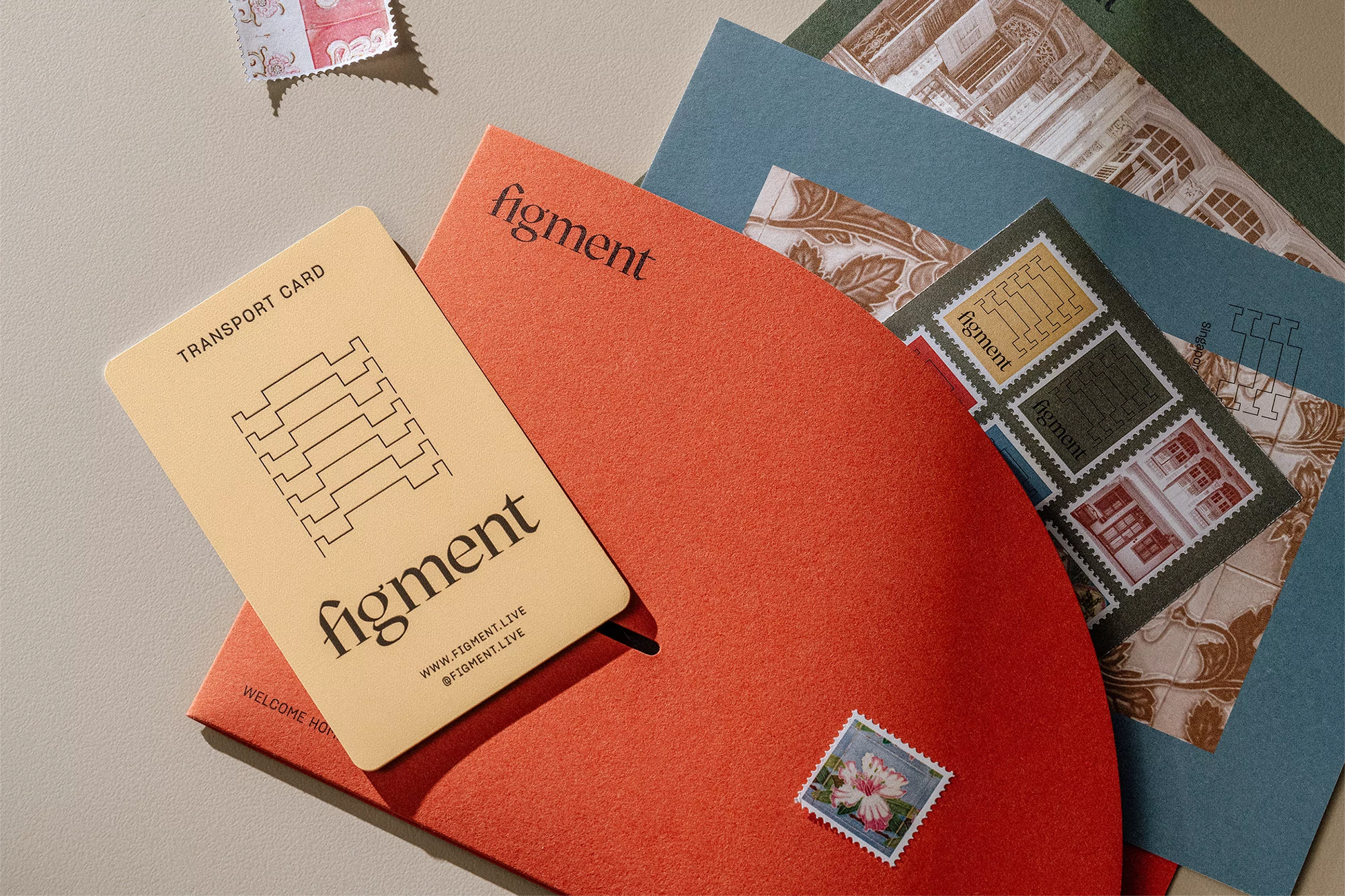Close-up of Figment branding on business card, red stationery, and vintage postage stamps on a neutral surface. Modern design.