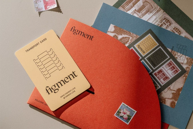 Close-up of Figment branding on business card, red stationery, and vintage postage stamps on a neutral surface. Modern design.
