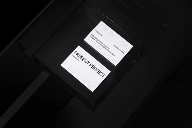 High-contrast monochrome studio flat lay showing business cards with minimalist typography on a dark reflective surface.