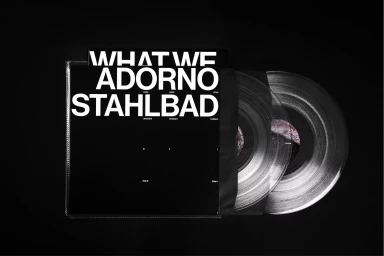 Black vinyl record sleeve with bold white typography next to two transparent vinyl records on dark background