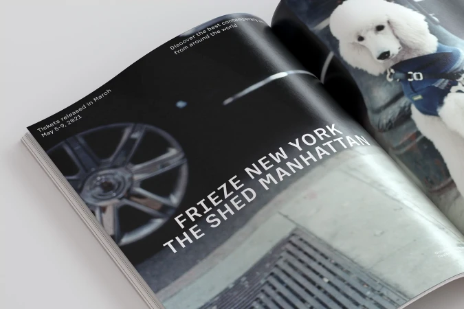 Magazine open featuring art fair advertisement with an image of a poodle wearing a harness and information about tickets.
