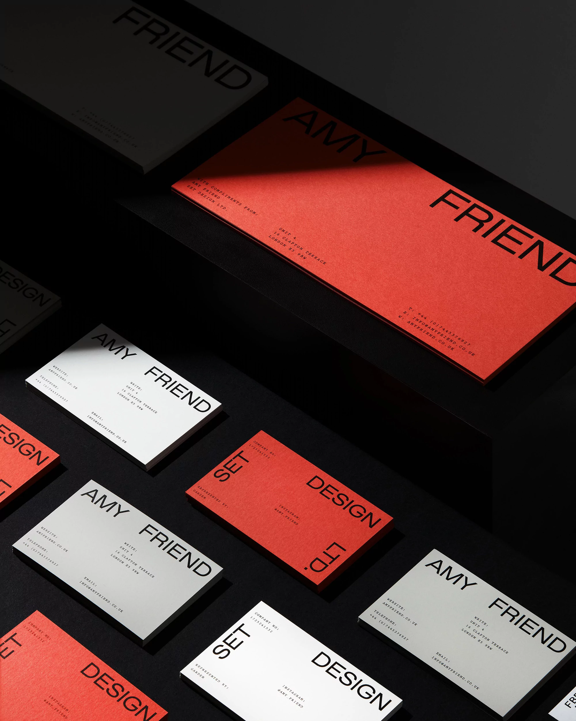 Arrangement of red and white business cards with minimalist typography on a dark surface, highlighted by a directional light source.