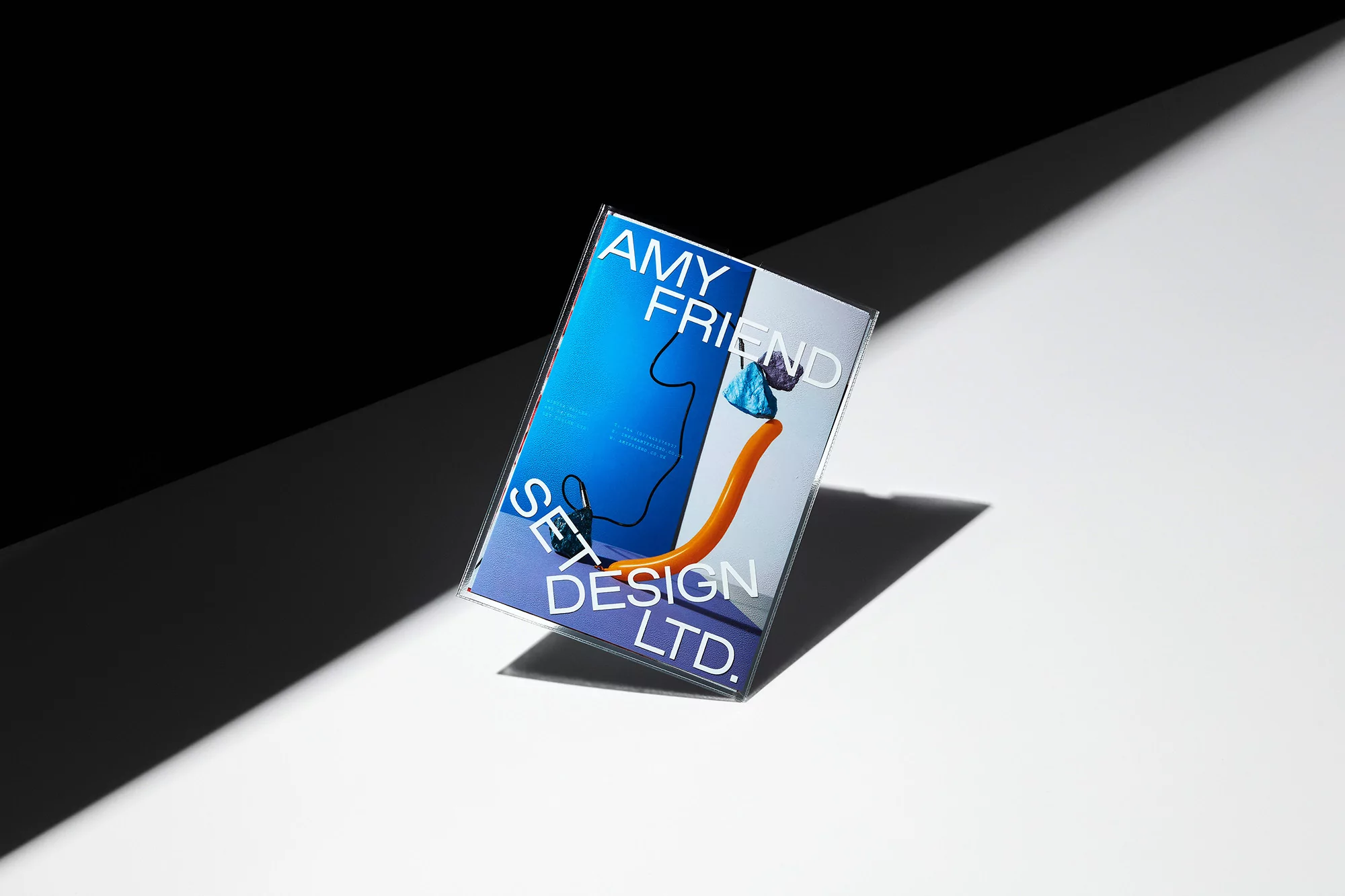 Graphic design portfolio book cover with geometric shapes and bold blue, orange, and white colors in a studio product shot.