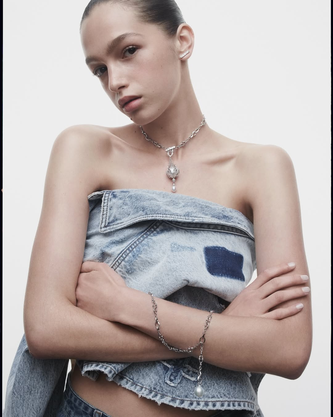 Model wearing a strapless denim top and silver pendant necklace against a plain white background