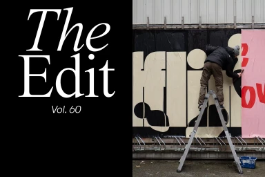 Person on a metal stepladder pasting large typographic posters on an outdoor wall next to large black typography on black