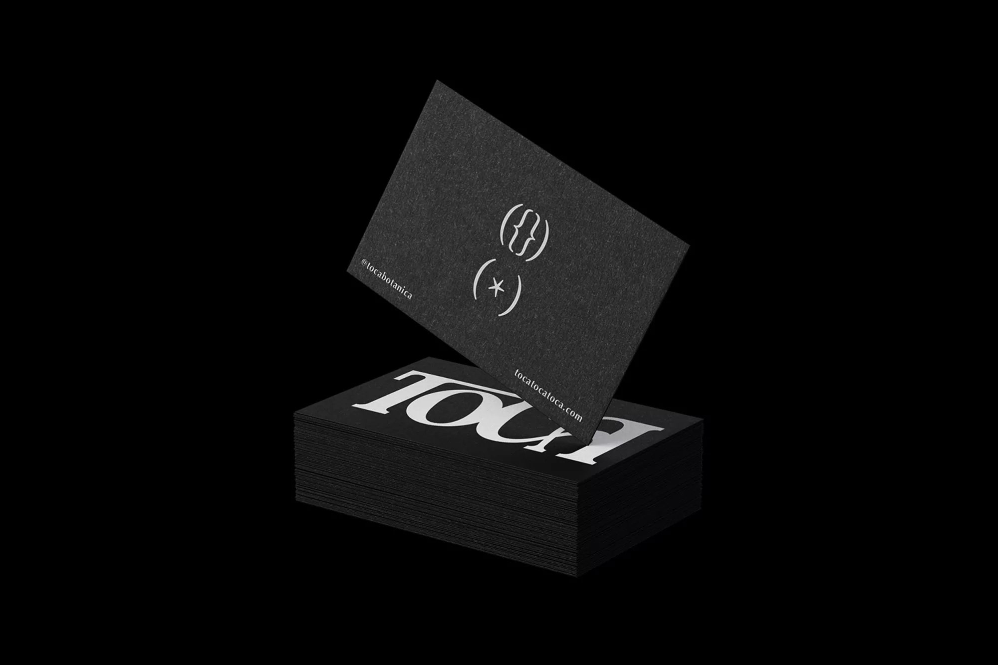 Black business cards featuring white typography and symbols stacked on a dark background with one card lifted above