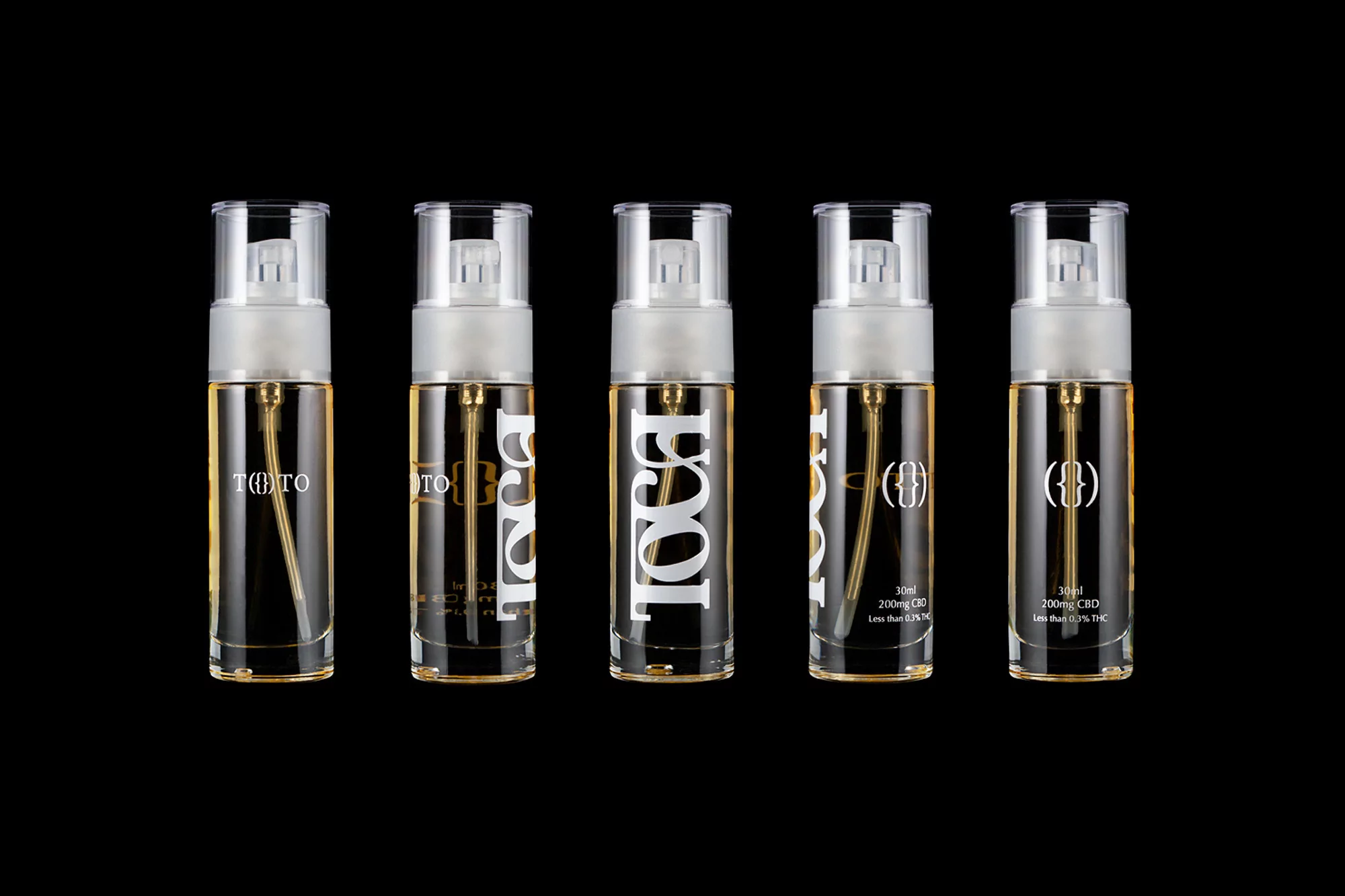 Five transparent bottles of oil with white labels and spray nozzles arranged on a black background, product photography.