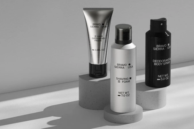 Silver tube of hair paste, white shaving foam bottle, and black deodorant spray on concrete pedestals in a high-key product shot.