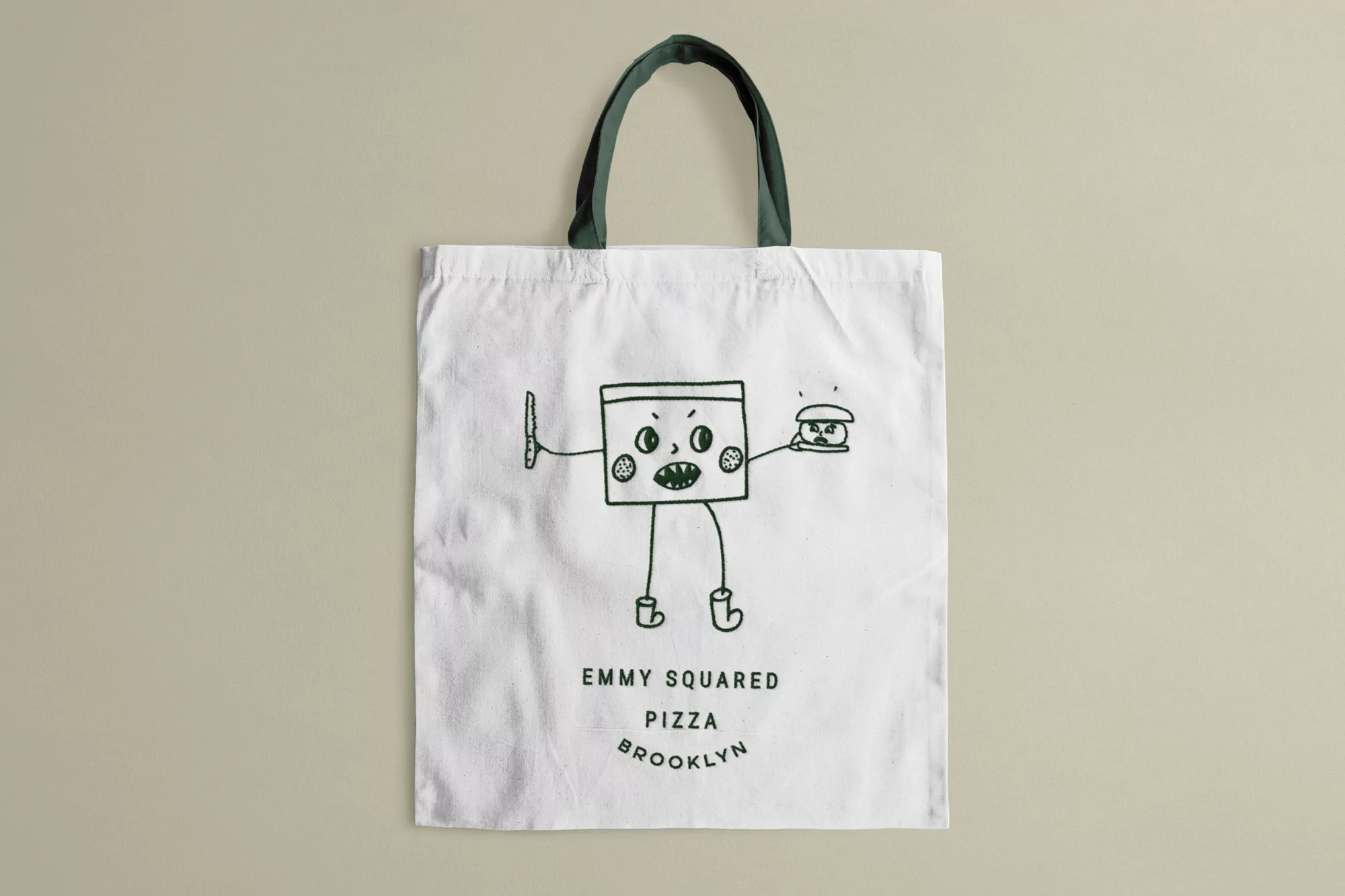 Canvas tote bag featuring cartoon monster graphic holding pizza burger with brand text, promoting Emmy Squared Pizza Brooklyn.