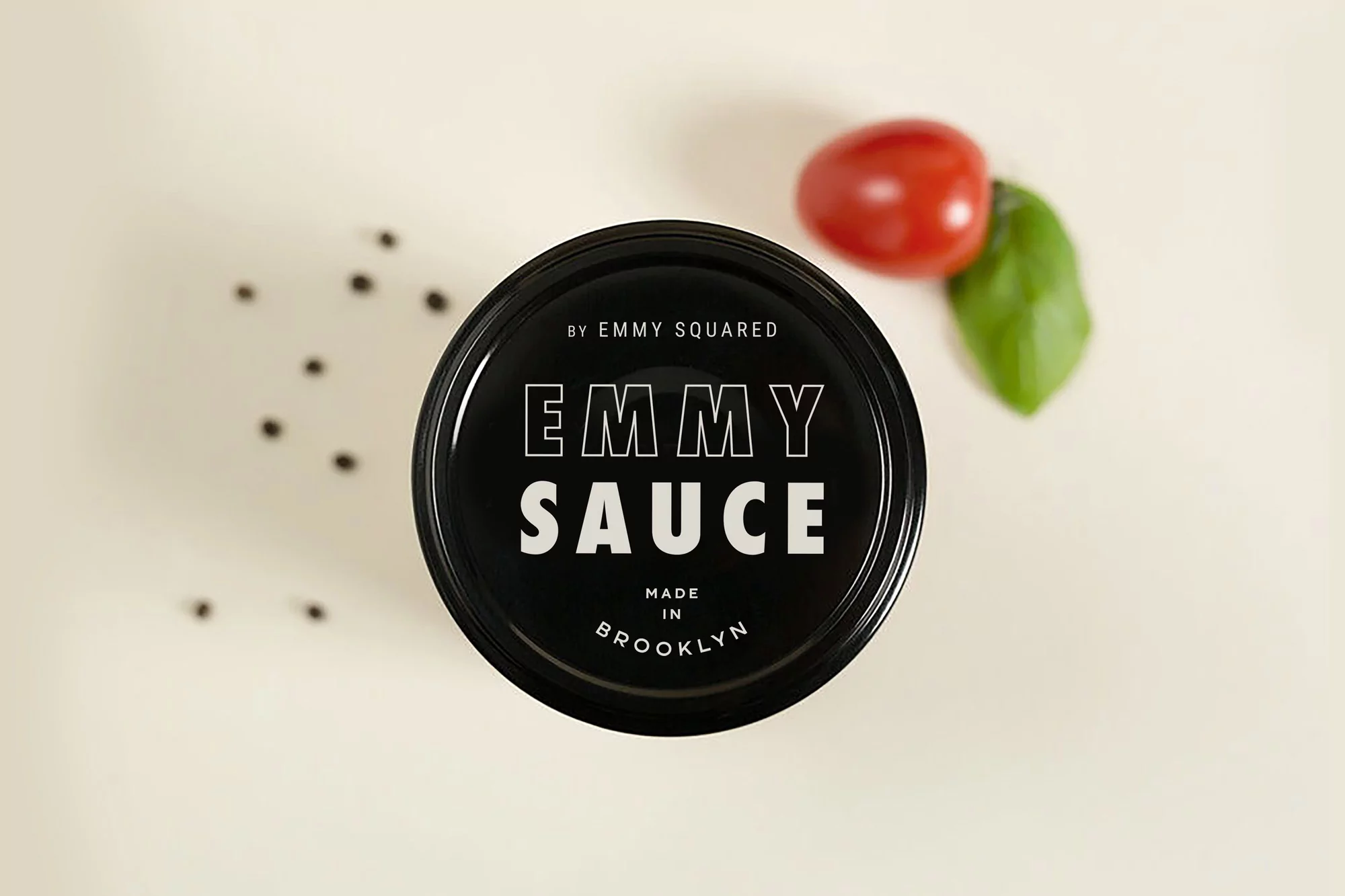 Emmy Sauce jar close-up with tomato and basil leaf on a cream background, showcasing simple food product presentation.