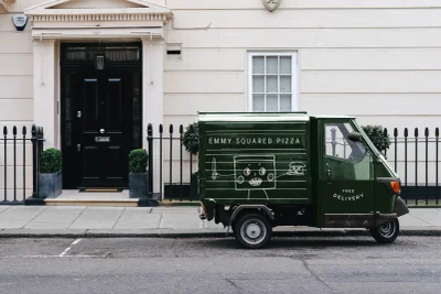 Green delivery truck parked on a city street in front of a classic building exterior with a black door