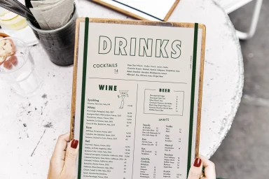 Hands holding a restaurant drinks menu clip board with green typography on a table