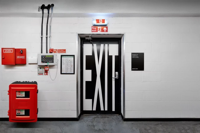 Emergency exit door with bold white letters, red fire safety equipment, and block wall in an indoor setting, creating a sense of security.