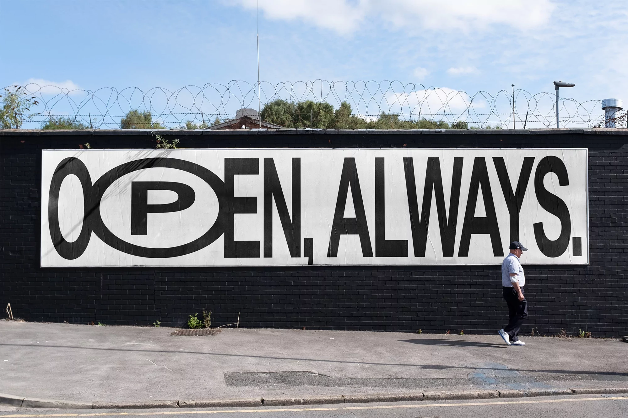 An outdoor scene featuring an adult wearing a cap walking past a black brick wall with a large white sign displaying 'OPEN, ALWAYS'.