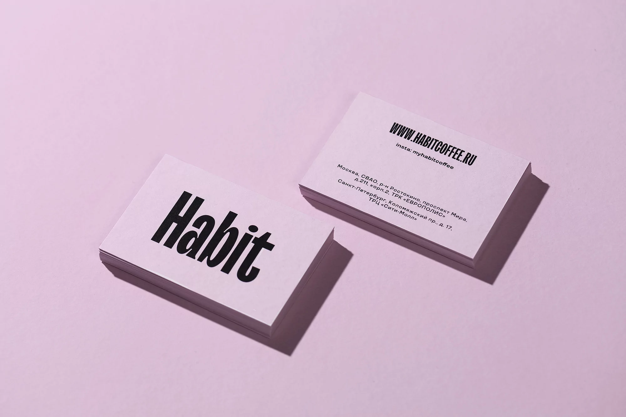 Stacks of white business cards with black text 'Habit' on a pink background. Minimalist branding design with website and address.