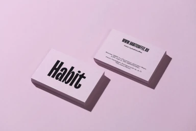 Two stacks of white business cards featuring bold black typography for Habit set against a soft pink background.