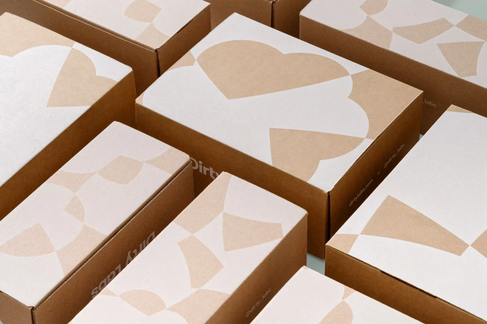 Group of tan and white cardboard shipping boxes with geometric patterns, stacked together on a pale green surface indoors.