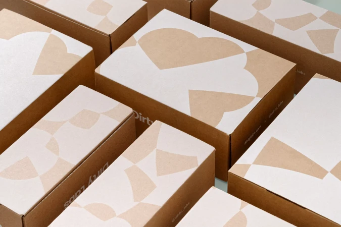 Group of tan and white cardboard shipping boxes with geometric patterns, stacked together on a pale green surface indoors.