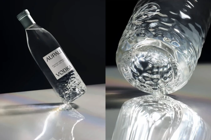 A clear glass bottle of Aupale Vodka is displayed on a reflective surface against a dark background in a product shot. 