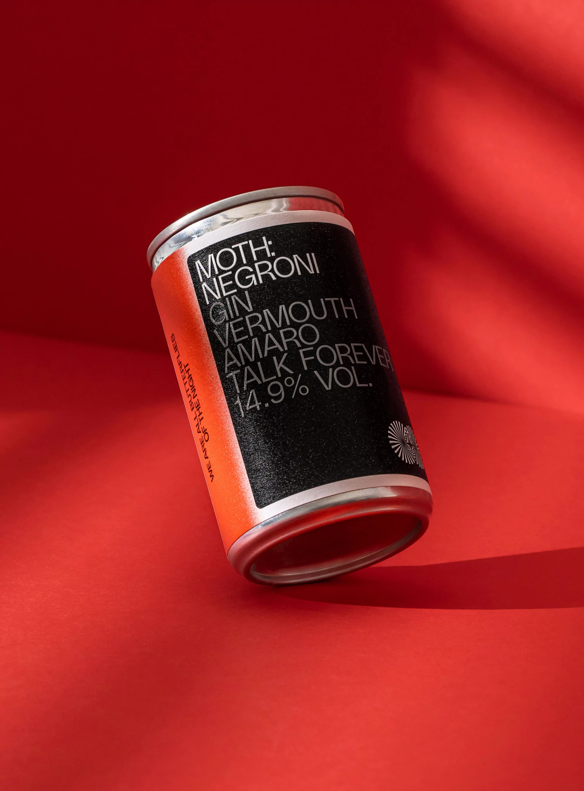 Studio shot of a Moth Negroni canned cocktail on a red background with abstract light patterns. Cocktail can is angled slightly.