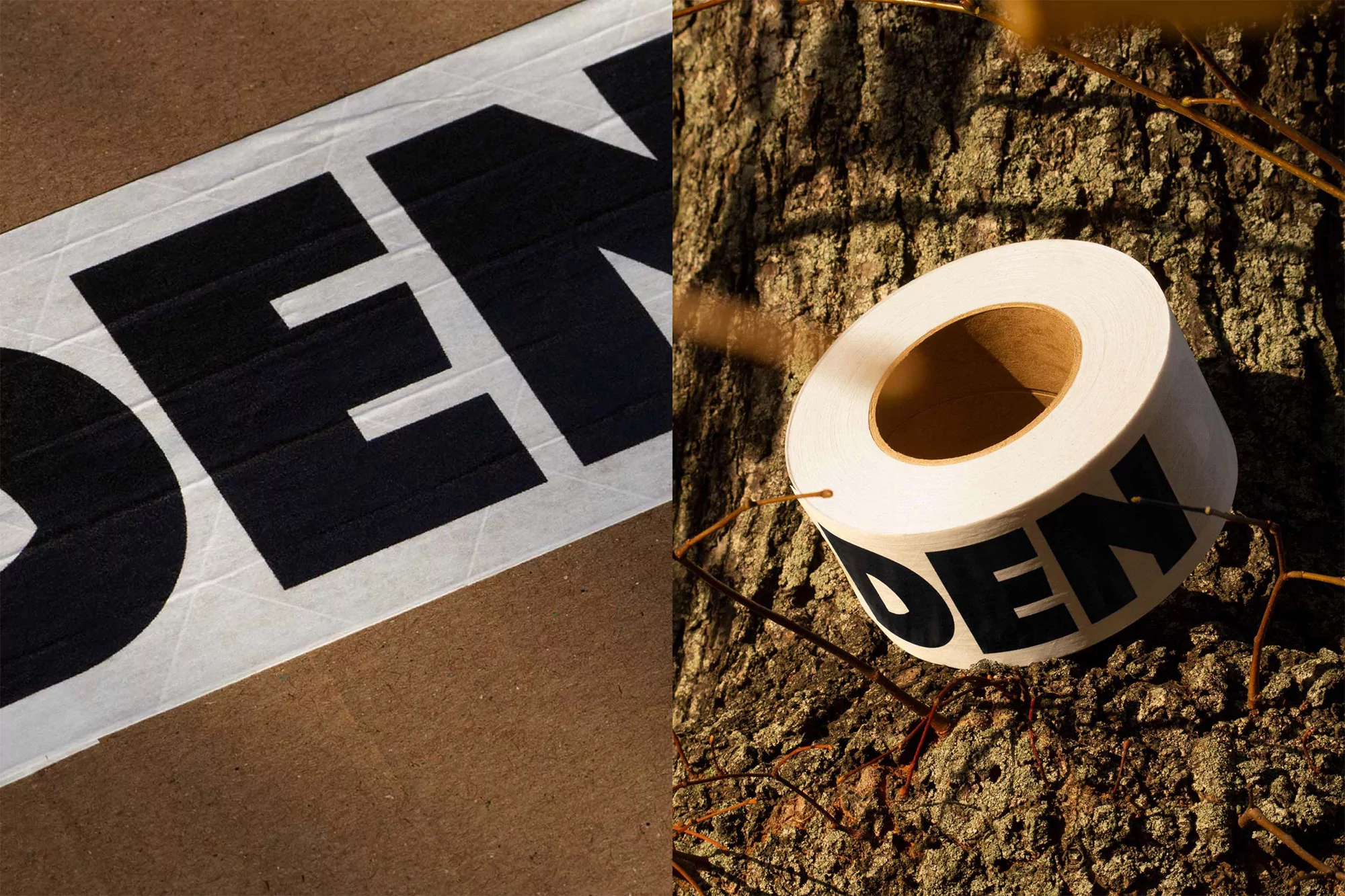 Roll of masking tape with the letters "DEN" resting on a tree trunk beside a section of tape on a cardboard surface.