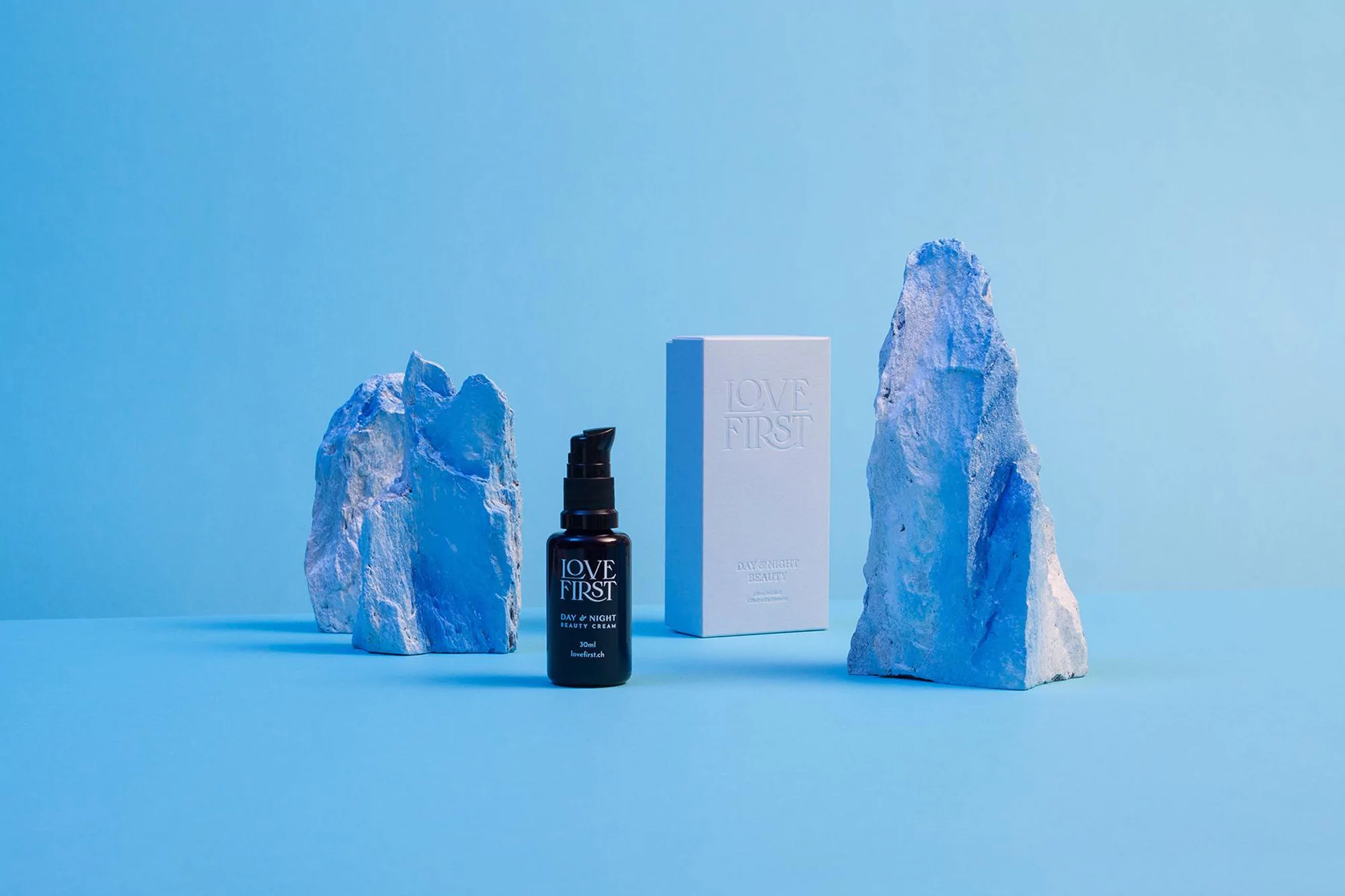 Product shot of black pump bottle and white box with blue-toned rocks on a light blue surface against a matching light blue background.