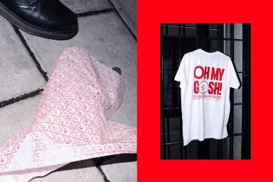 White t-shirt with red printed typography hanging on a dark metal gate against a bright red background.