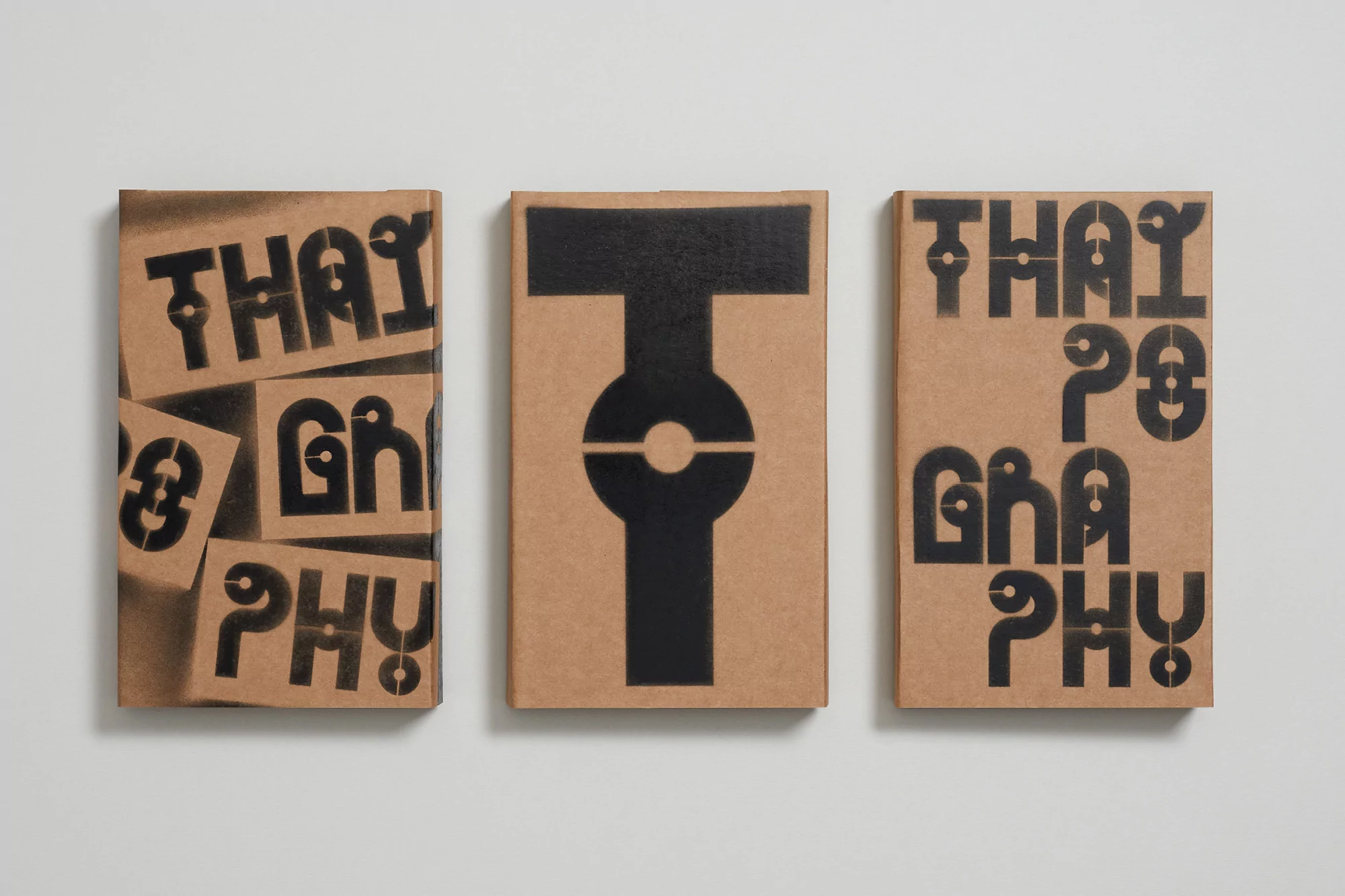 Three tan colored book covers with black stencil typography sit side by side against a white background in a studio shot.