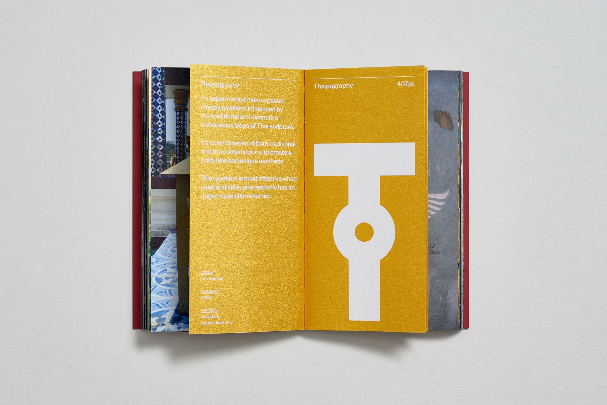 Open book displaying a white typographic character on a gold background, featuring the word 'Thaipography' in a sans-serif font.