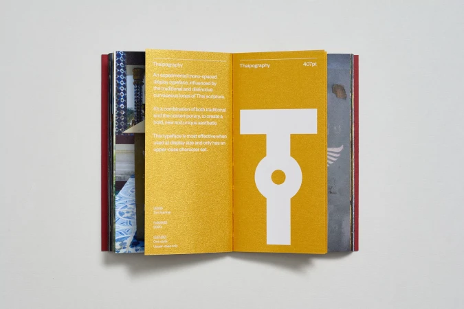 Open book displaying a white typographic character on a gold background, featuring the word 'Thaipography' in a sans-serif font.