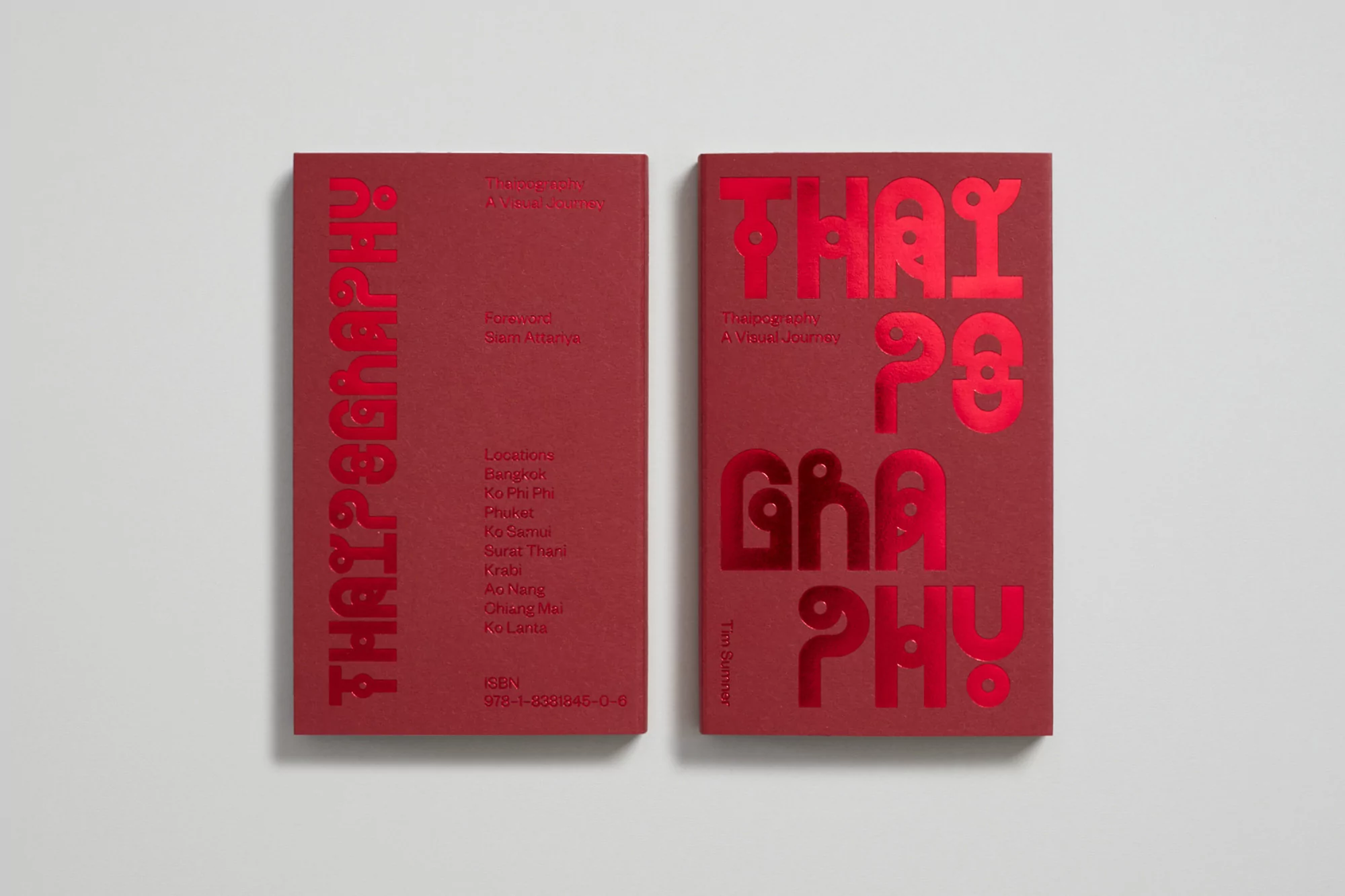 Close-up of two red hardcover books titled "THAYPOGRAPHY", featuring details such as the foreword, locations, and ISBN. Neutral background.
