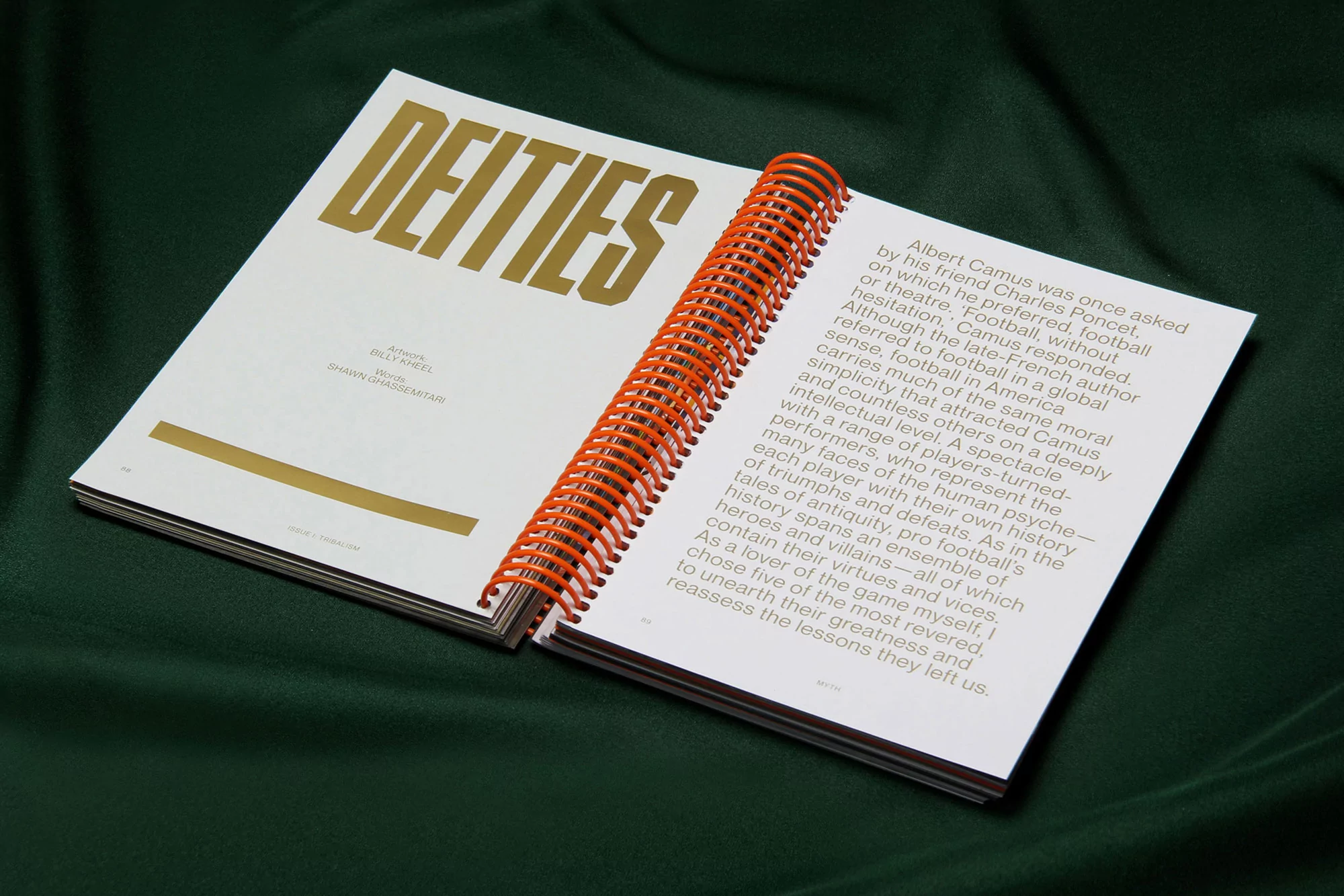 Open book with orange spiral binding displays 'DEITIES' in gold font against white, resting on a dark green velvet background.