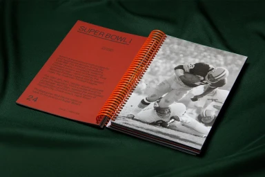Open spiral-bound book with a red editorial page and a black and white football photo resting on dark fabric.