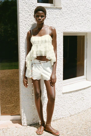 Model standing outdoors against a textured white wall wearing a pale yellow top and white shorts for Zara