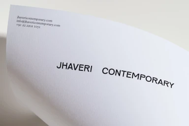 Curved sheet of white textured paper featuring printed typography for Jhaveri Contemporary brand identity