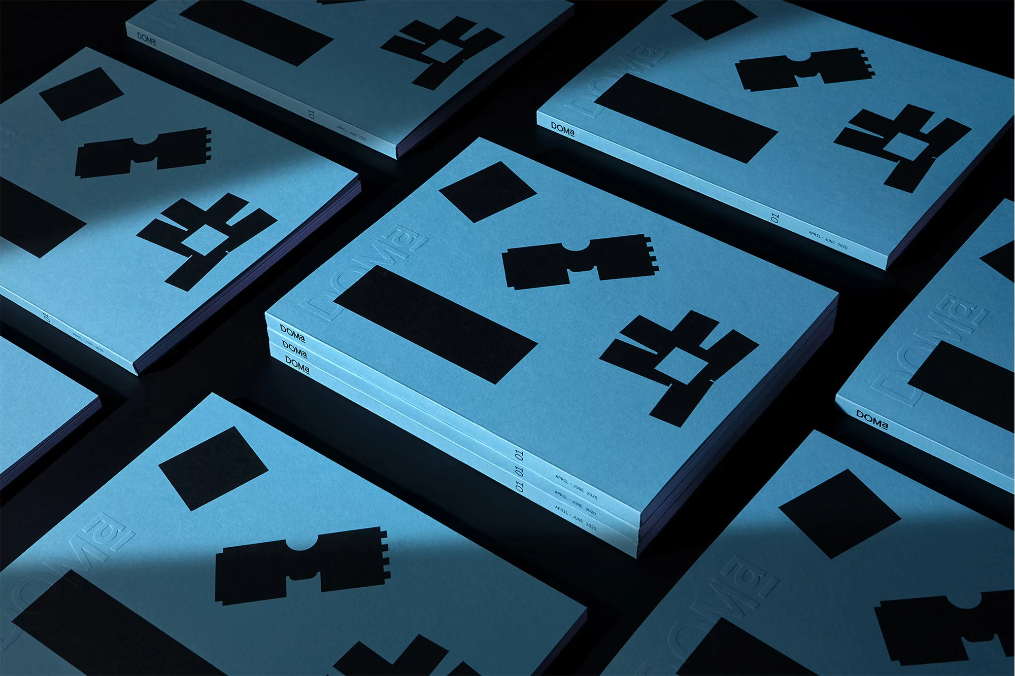 Arrangement of several light blue magazines or books with graphic black shapes and embossed text, creating an abstract design.