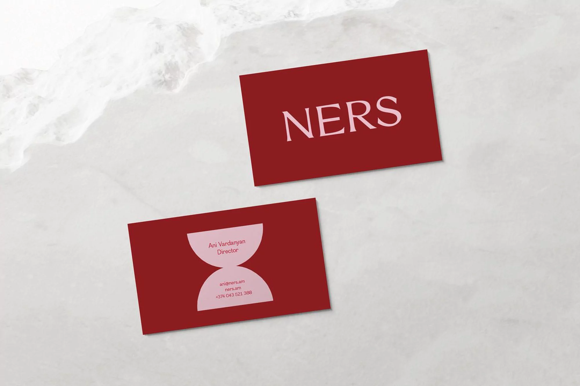 Two maroon business cards on a white marble surface, one with 'NERS' printed in light pink, the other with company details.