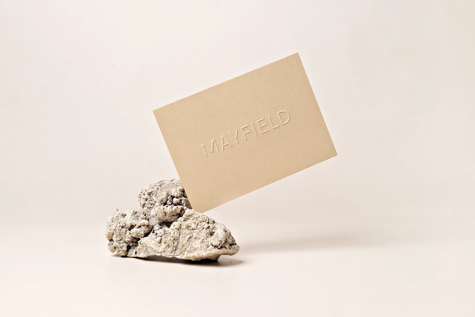 Minimalist still life of a beige card with debossed text balanced on a textured stone against a soft, neutral backdrop.