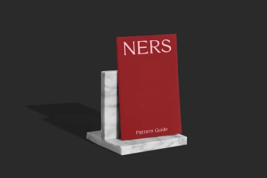 Red book titled Ners Pattern Guide standing upright in a white marble bookend against dark grey background.