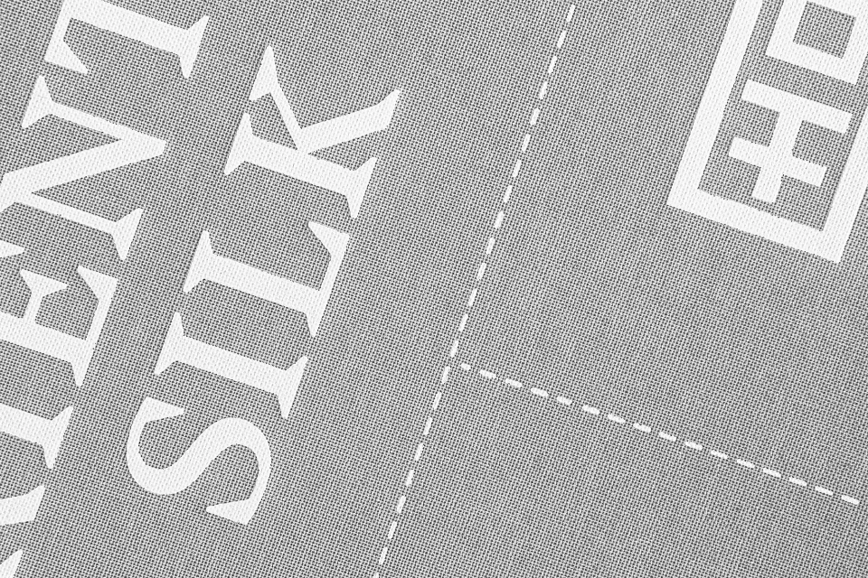 Close-up of grey fabric with white text reading 'TEXTILE EVENT SILK' and a white logo in the upper right corner.